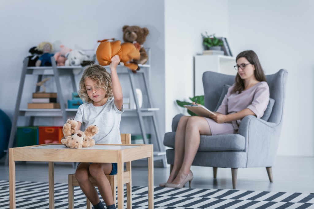 a little girl sitting at a table with a teddy bear